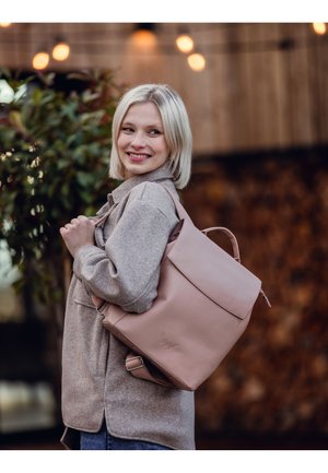 Light pink leather backpack with a structured design, featuring a flap closure and adjustable straps. Soft texture and minimalistic logo detail.