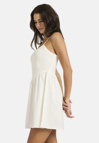 Λευκό φόρεμα με σφηκοφωλιά σε κολλητό μπούστο και λεπτές τιράντες. Διαθέτει φαρδύ, ρέον φούστα και απαλό, υφασμάτινο ύφασμα με υφή, που ενισχύει την ελαφριά του εμφάνιση.