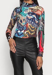 Haut à manches longues et col roulé avec un motif abstrait multicolore comprenant des tons bleus, rouges et terreux. Tissu doux avec une coupe ajustée.