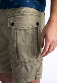 Shorts en kaki en coton texturé, dotés de deux poches latérales, d'une poche arrière avec fermeture à bouton et de détails de couture visibles.