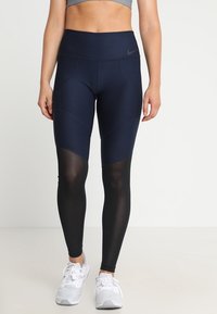 Granatowe legginsy sportowe z wysokim stanem, z czarnymi siateczkowymi panelami na dolnych partiach nóg oraz subtelnym wykończeniem szwów.