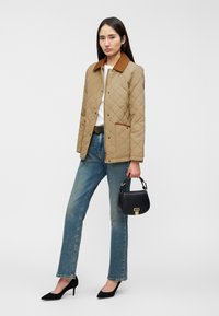 Ανοιχτό καφέ μπουφάν με καπιτονέ σχέδιο και καφέ γιακά, συνδυασμένο με ανοιχτό μπλε τζιν. Μαύρη τσάντα χειρός και τακούνια ολοκληρώνουν την εμφάνιση.