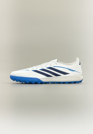 Χαμηλού προφίλ λευκό αθλητικό παπούτσι Adidas Copa με μπλε σόλα και μαύρες ρίγες, σχεδιασμένο για ποδόσφαιρο σε τεχνητό χλοοτάπητα ή σε εσωτερικούς χώρους.