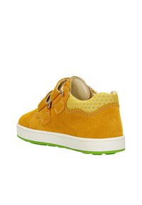 Sneaker giallo in suede con un pannello di tessuto giallo testurizzato, doppie cinghie in Velcro, suola bianca e dettagli verde sulla suola esterna.
