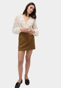 Witte blouse met gerimpelde halslijn en aantrekkoord, gecombineerd met een bruin mini-jurk. Zwarte instapschoenen maken de look compleet. Glad textuur overal.