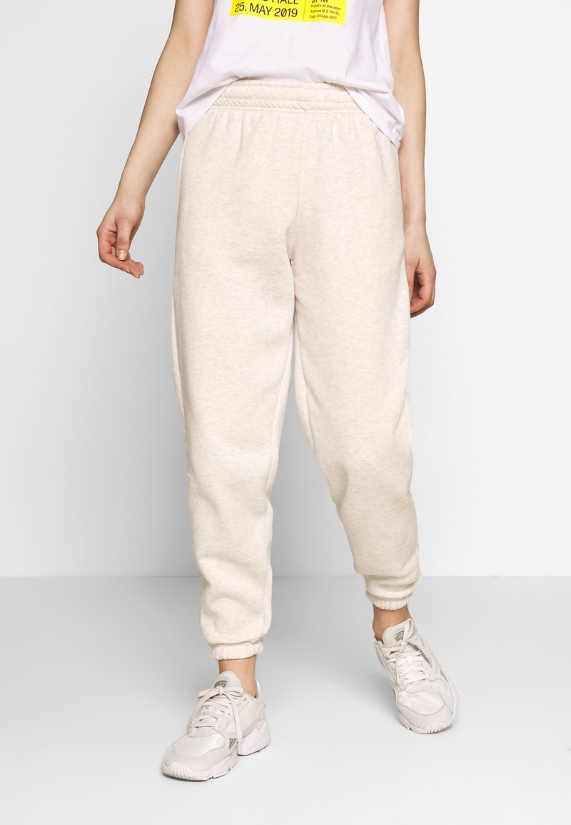 Beige trainingsbroek van zacht materiaal, met een relaxte pasvorm, elastische tailleband en geribbelde manchetten. Gemaakt in combinatie met lichte sneakers.