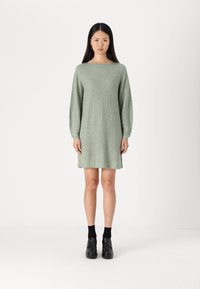 Robe pull tricotée en vert clair avec un col rond, des manches longues et une coupe décontractée. Présente un tissu texturé et un ourlet long jusqu'aux genoux.