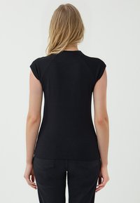 Schwarzes, tailliertes Shirt mit kurzen Ärmeln, aus weichem, elastischem Stoff gefertigt. Verfügt über einen runden Ausschnitt und eine glatte, einfarbige Textur.