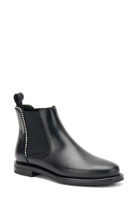 Stivaletto Chelsea in pelle nera con pannelli elastici laterali, texture liscia e dettagli in metallo argentato lungo la cucitura. Suola nera spessa con un leggero tacco.