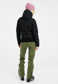 Abgeschnittene schwarze Daunenjacke mit Kapuze, kombiniert mit olivgrünen Hosen. Die Jacke hat einen gerippten Saum und die Hosen verfügen über Reißverschluss an den Knöcheln.