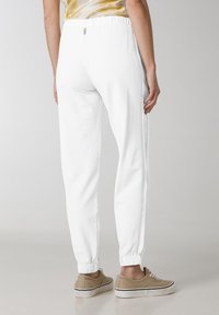 Vita sweatpants med elastisk midja och muddar, med sidostreck och avslappnad passform. Matchas med ljusbruna sneakers.