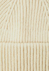 Gorro de punto color crema con textura acanalada, que presenta fibras claras y oscuras alternas para un patrón sutil. Material suave y cálido.