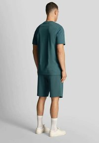 Set composto da t-shirt e pantaloncini in cotone verde acqua, con vestibilità rilassata. Modello di spalle, mostra maniche corte e design semplice senza motivi visibili.
