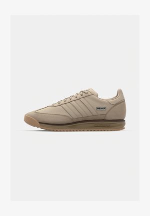 Sapatilhas atléticas bege com acabamento em camurça, apresentando três riscas paralelas, sola de borracha e detalhes texturizados no calcanhar.