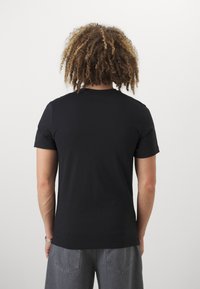 Svart kortermet t-skjorte laget av bomull, med rund hals. Baksiden har en jevn tekstur og minimal design uten pynt.