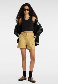 Svart ribbad crop top, khaki cargo shorts med två fickor, svart varsity-jacka, leopardmönstrade slip-on-skor, svarta strumpor.