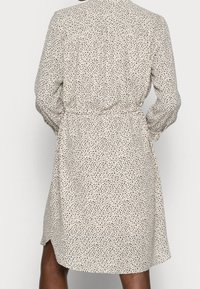 Helles beiges Kleid mit schwarzen Pünktchen, langen Ärmeln, raffen Bündchen und gebundenem Taillenband, mit einem knielangen Saum und seitlichen Schlitzen.