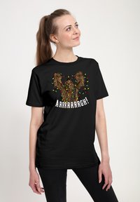 T-shirt noir présentant un graphisme d'une créature avec les bras levés, ornée de lumières de fête colorées, et le texte "ARRRRRRRRGH!" en dessous.