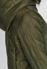 Prošívaná olivově zelená bunda s kapucí, která má diamantové vzory, hladkou texturu a detaily na postranních švech.