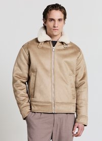 Giacca con colletto in shearling beige, chiusura con zip, due tasche frontali e una texture liscia. Presenta una vestibilità comoda e dettagli hardware minimalisti.