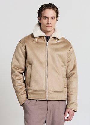 Giacca con colletto in shearling beige, chiusura con zip, due tasche frontali e una texture liscia. Presenta una vestibilità comoda e dettagli hardware minimalisti.