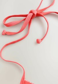 Korall színű textil hevederek masniban megkötve, sima felülettel és lekerekített végekkel, világos háttér előtt.