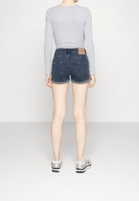 Tummansiniset farkkushortsit, joissa on käännetty helma ja kaksi takataskua, yhdistettynä harmaaseen pitkähihaiseen puseroon ja hopeisiin lenkkareihin.