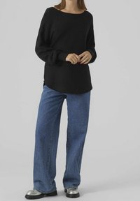Pull en tricot noir avec un large décolleté, assorti à un jean ample bleu clair et des chaussures à plateforme argentées. Texture lisse et coupe décontractée.