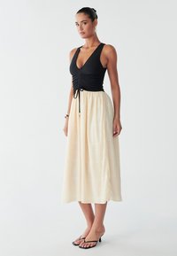 Svart figurnära topp med djup V-ringning och rynkning, kombinerad med en luftig midi-kjol i krämfärg med ett texturerat mönster och dragsko i midjan.