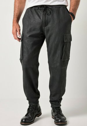 Uomo che indossa pantaloni cargo jogger neri con polsini elastici e stivali neri allacciati, in piedi con le mani rilassate ai lati.