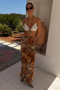 Bralette di paillettes argento, abbinato a una lunga gonna a stampa tigre arancione e nera. La texture è liscia; l'outfit è completato da collane a strati.