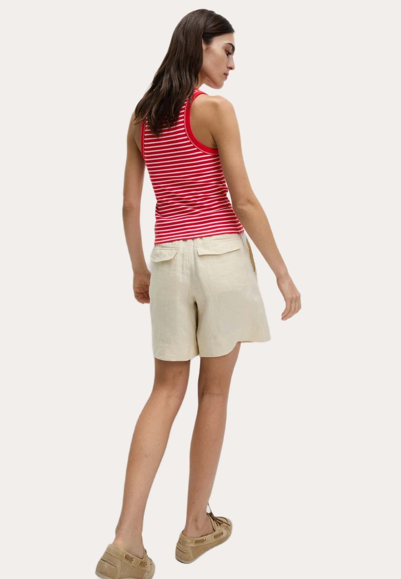 Canottiera a righe rossa e bianca abbinata a pantaloni corti di lino beige, con due tasche posteriori e una vestibilità comoda. Indossata con scarpe marrone chiaro.