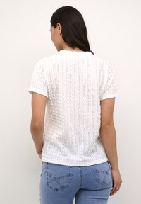 Bílý texturovaný top s krátkým rukávem a žebrovaným vzorem, kulatým výstřihem, doplněný světle modrými slim fit džíny. Viditelné detaily na lemu a rukávech.