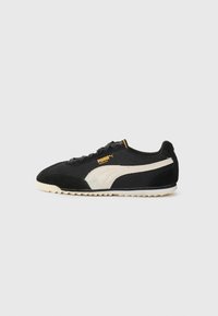 Zapatillas negras de materiales de malla y gamuza, con una franja blanca lateral y un logo amarillo. Suela texturizada para mayor tracción.