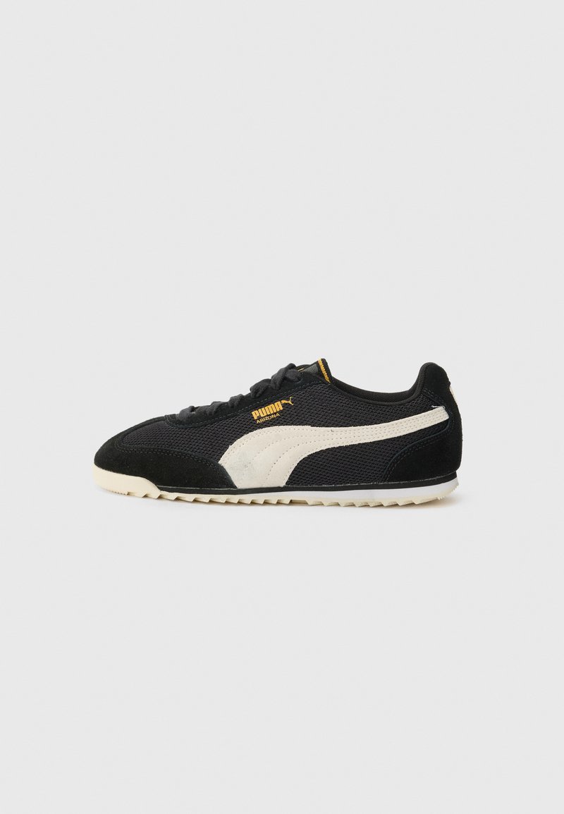Zapatillas negras de materiales de malla y gamuza, con una franja blanca lateral y un logo amarillo. Suela texturizada para mayor tracción.