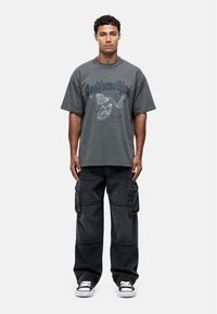 Grijze oversized t-shirt met vlinderafbeelding en tekst, gecombineerd met zwarte cargobroeken met zijzakken en sneakers.