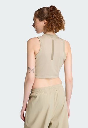 Beige cropped toppi, jossa pyöreä pääntie ja ohut pystysuora yksityiskohta takana. Yhdistetty samaa materiaalia oleviin housuihin, joissa on joustava vyötärönauha.