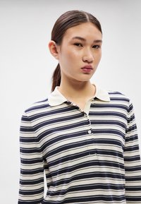 Tricou polo cu mânecă lungă, cu dungi alb-crem și bleumarin, guler clasic și fante cu nasturi. Material moale, cu dungi drepte și uniforme.