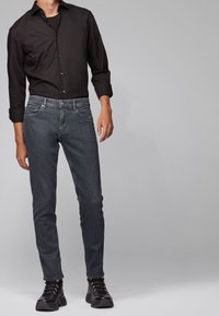 Black button-up shirt paired with dark gray slim-fit jeans and black lace-up boots, presenting a clean, modern casual outfit.