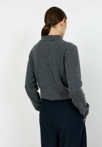 Šedý vlněný svetr s límečkem, slim fit a dlouhými rukávy, doplněný o tmavé pruhované kalhoty. Měkká textura, minimalistický design.