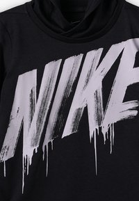 Musta huppari, jossa on suuri, kulunut valkoinen Nike-logo rinnan kohdalla, kauluksellinen muotoilu ja pehmeä textura.