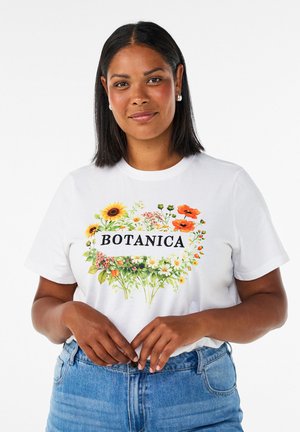 Femme aux cheveux mi-longs foncés portant des boucles d'oreilles en perles, un t-shirt blanc avec des fleurs colorées et le mot "BOTANICA," et un jean bleu.