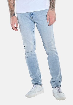 Hellblaue Denimjeans im Slim Fit, mit einem verwaschenen Finish und dezenten Abnutzungserscheinungen. Kombiniert mit weißen Sneakers und einem schlichten Hemd.