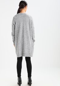 Gray knit cardigan with long sleeves, mid-thigh length, side pockets, and a relaxed fit, paired with black slim pants and ankle boots.