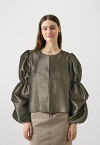 Top grigio metallizzato testurizzato con maniche a sbuffo, scollatura rotonda e chiusura con zip anteriore. Abbinato a una gonna beige chiaro, senza motivi visibili.