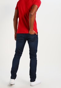 Red short-sleeve t-shirt paired with dark blue fitted jeans and white sneakers. The outfit features a simple, casual design and fit.