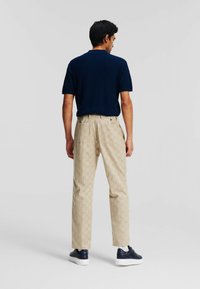 Navy textured short-sleeve polo and beige patterned trousers. Sneakers with a smooth finish. Back view shows fit and design details.