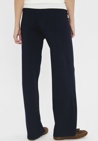 Tengerészkék, laza szabású nadrág, puha tapintással és széles lábakkal, bordázott derékkal és enyhén rövidített hosszal.