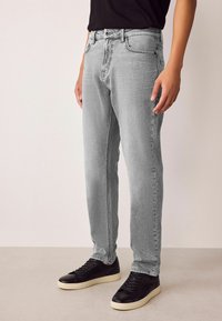 Blugi gri din denim cu un croi drept și o textură subtilă, asortați cu teniși negri având o talpă contrastantă.