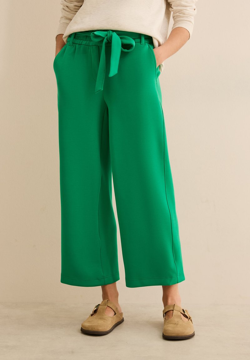 Pantalons larges verts avec une taille élastique et un détail à nouer. Comprend des poches latérales et un tissu lisse et stretch. Coupe décontractée.